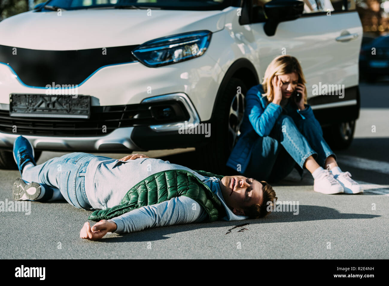 scared young woman calling emergency while injured man lying on road after traffic collision Stock Photo