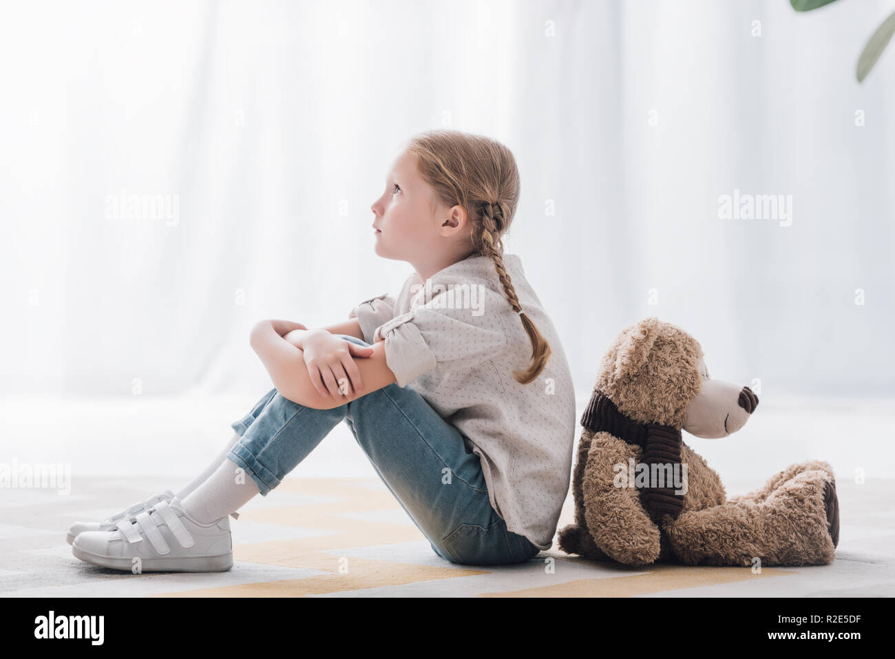side view of thoughtful little child sitting on floor back to back with ...
