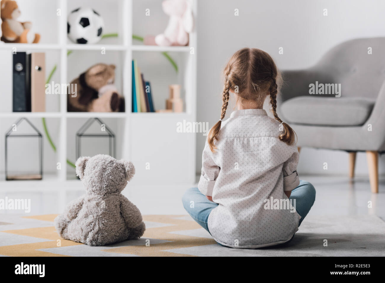 rear view of little child in white shirt sitting on floor with teddy ...