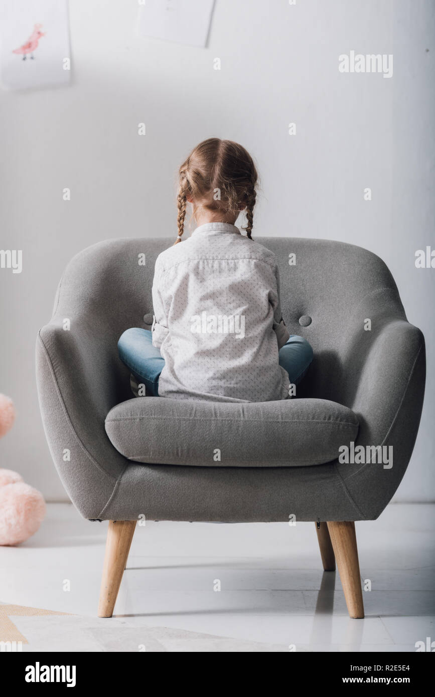 rear view of lonely little child sitting in armchair in front of white ...