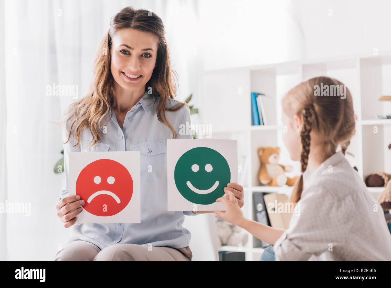 smiling psychologist showing happy and sad emotion faces cards to child Stock Photo