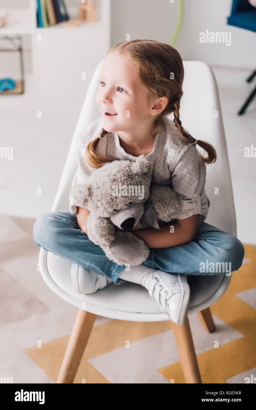 happy little child sitting on chair and embracing her teddy bear Stock ...
