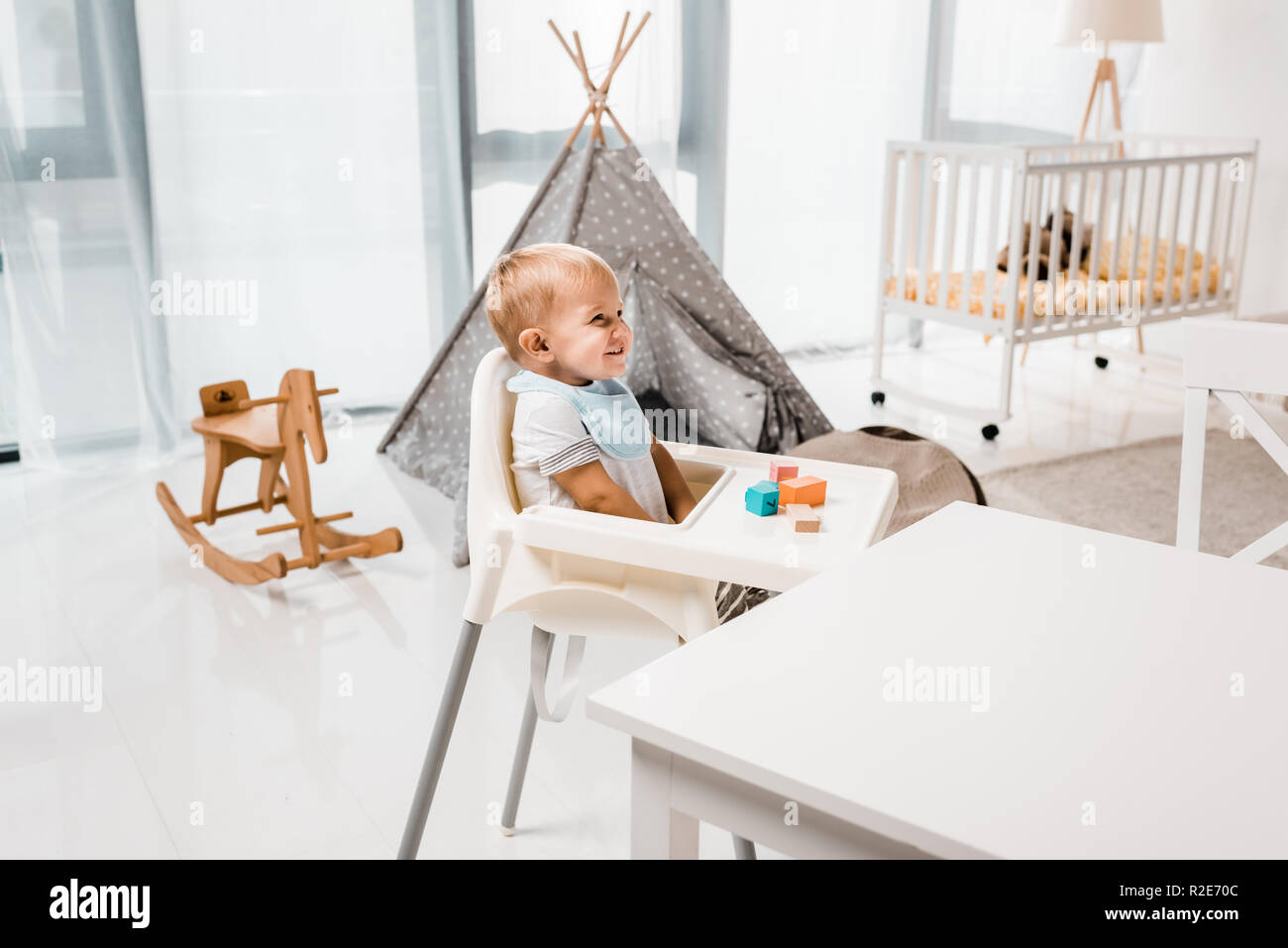 happy toddler sitting in baby chair in nursery room with toy cubes Stock Photo