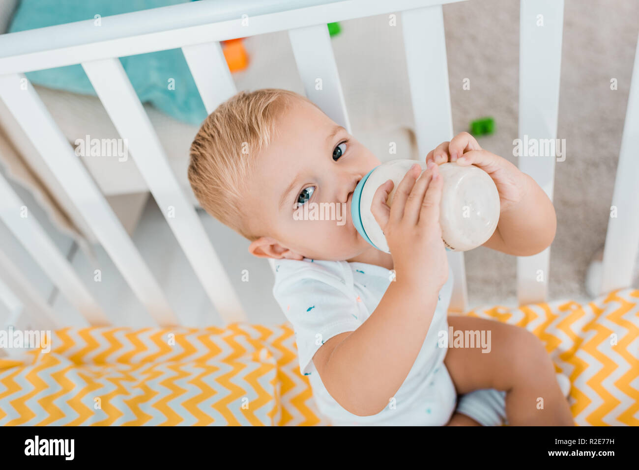 Adorable Toddler Drinking Out Of Baby Bottle In Crib Stock Photo