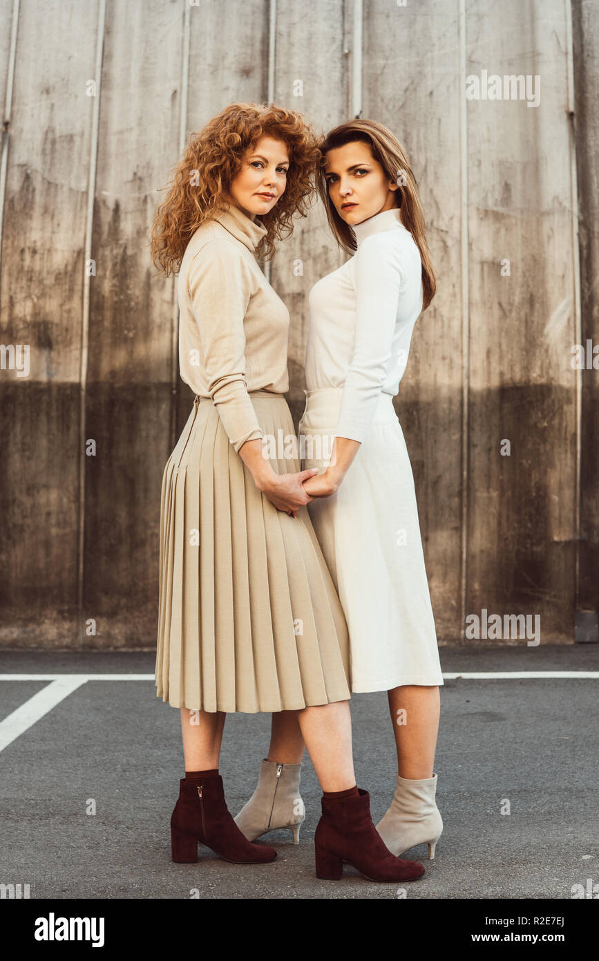 beautiful female models in turtle necks and skirts holding hands at urban street Stock Photo