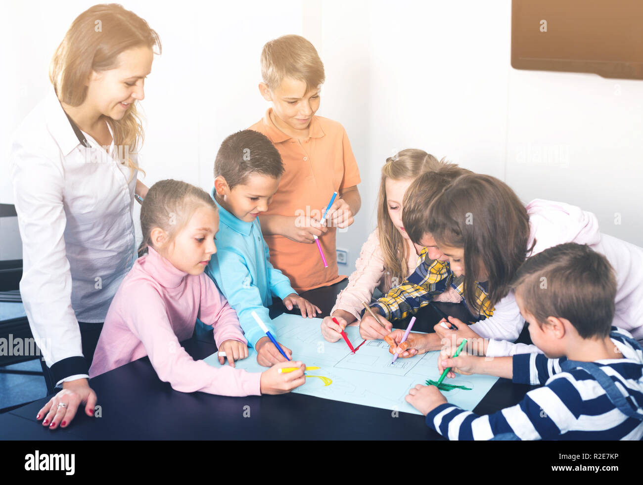 smiling professor and elementary age children drawing together one ...
