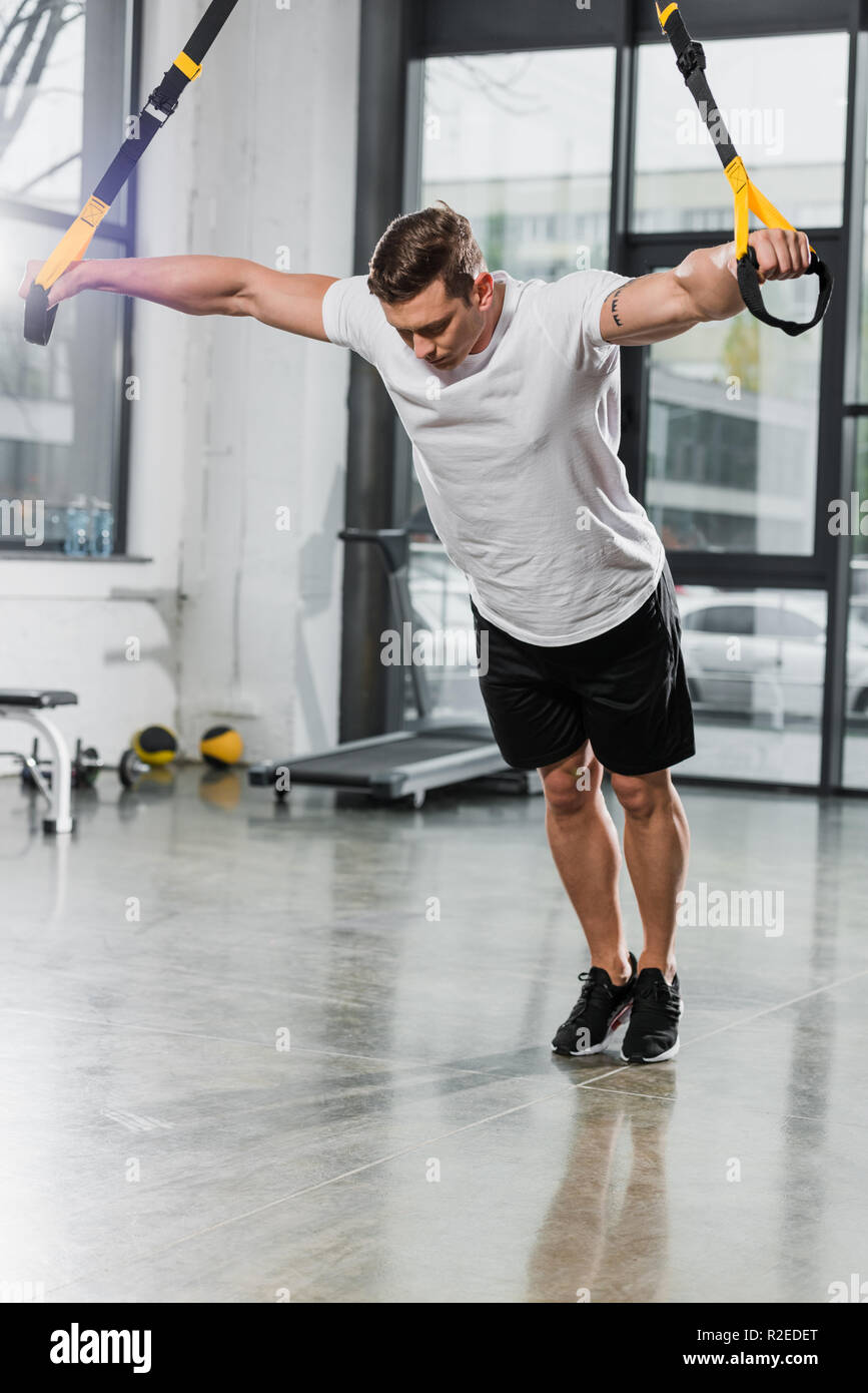 handsome muscular bodybuilder working out with suspension straps in gym