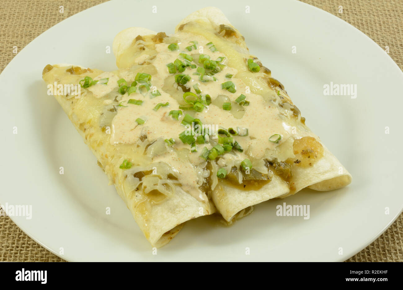 Chicken and bean salsa verde enchildas on plate with cheese and chopped green onions Stock Photo