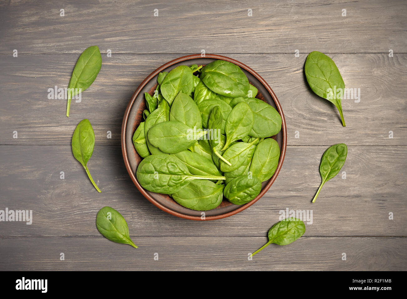 Green spinach leaves in brown bowl on dark leafy food background as a healthy eating concept of fresh garden produce organically grown as a symbol of  Stock Photo