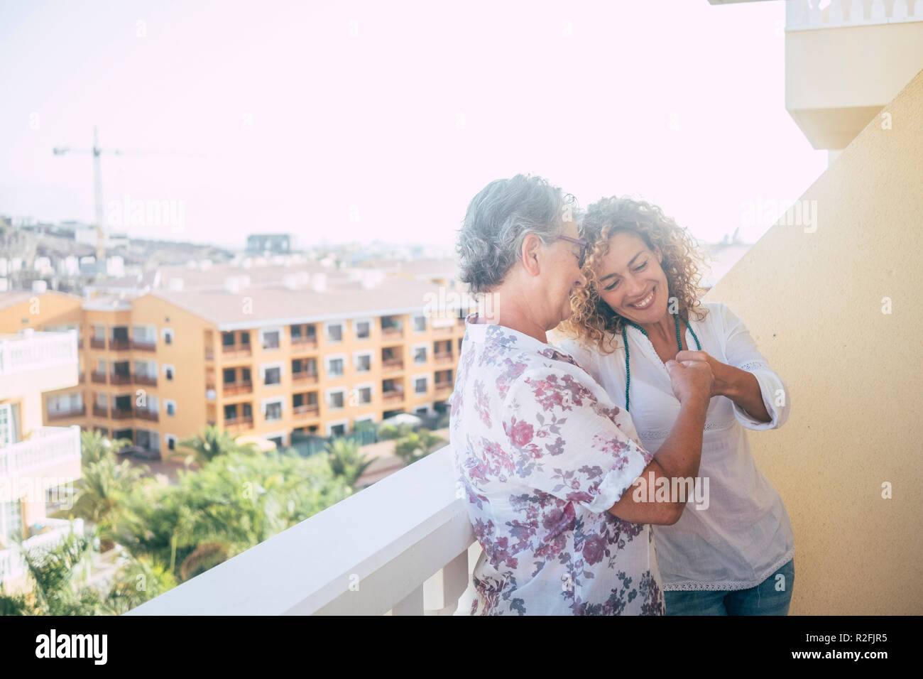 couple of women friends stay in the terrace together enjoying the friendship at home touching punch in real friendly way. cheerful adult and middle age women stay together and enjoy the life. city view from terrace Stock Photo