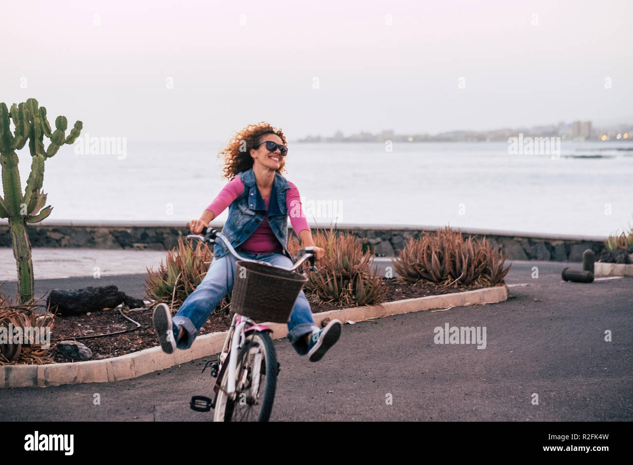 happiness and joyful for curly beautiful lady go on a bybicle opening legs and having a lot of fun. freedom and enjoying life concept with cheerful people in outdoor leisure activity. Stock Photo