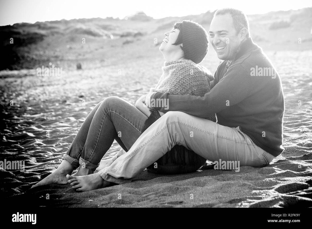 cute man and woman middle aged having fun in love at the beach outdoor. leisure activity and big smile and laugh for the lady. the man embrace her. rocks on the background Stock Photo