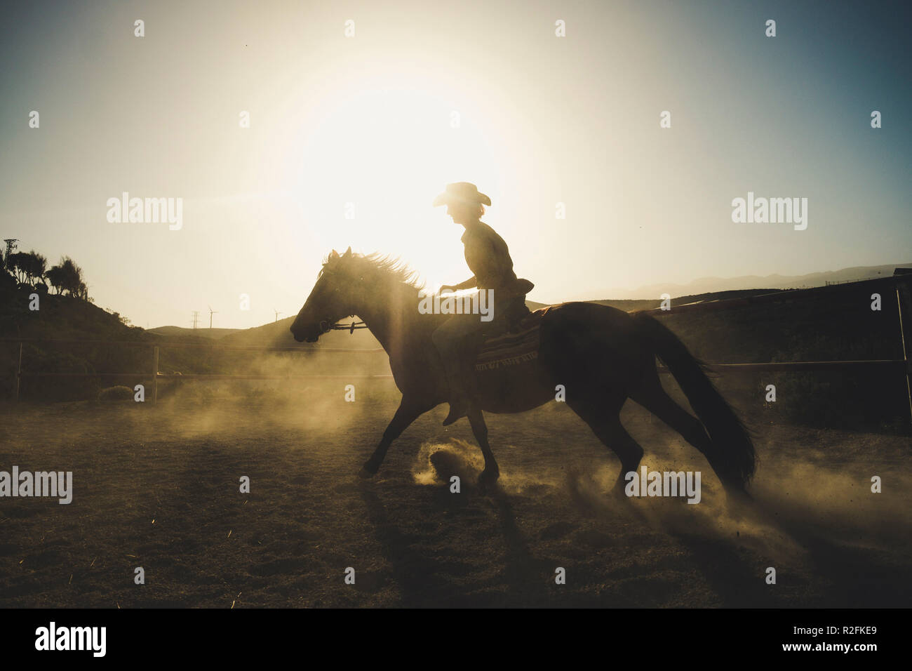 beautiful girl ride a horse in silhouette and backlight with sunflare and dust from the ground. epic and heroes image for speed and cowbot life and adventure concept. travel different lifestyle Stock Photo
