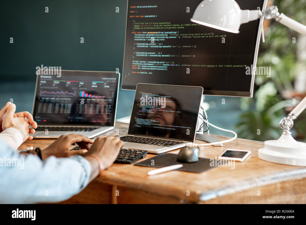 Programmers writing a program code sitting at the workplace with three monitors in the office. Cropped imaage with no face Stock Photo