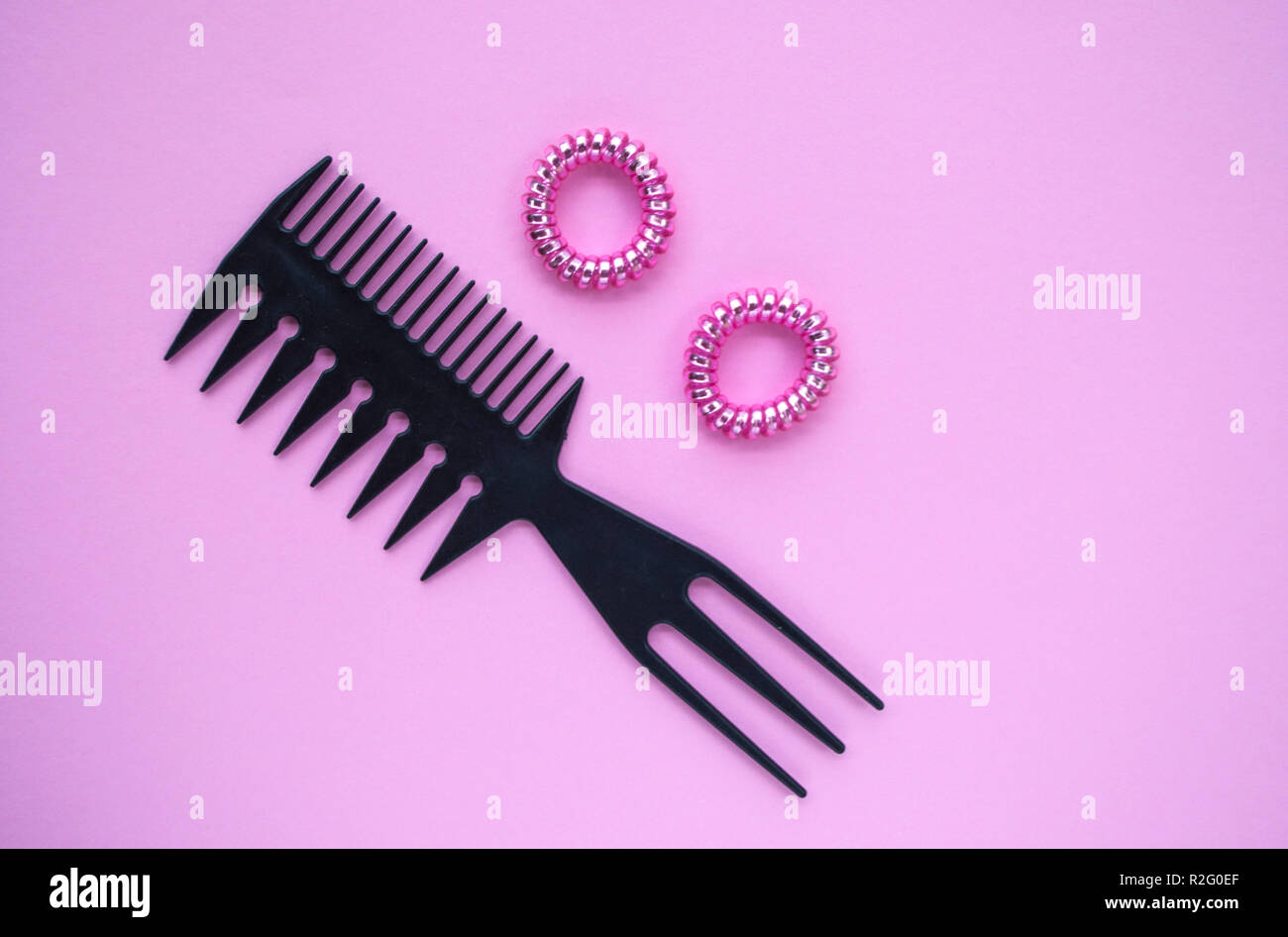Black plastic comb and two pink shiny scrunchies on pastel pink background. Stock Photo
