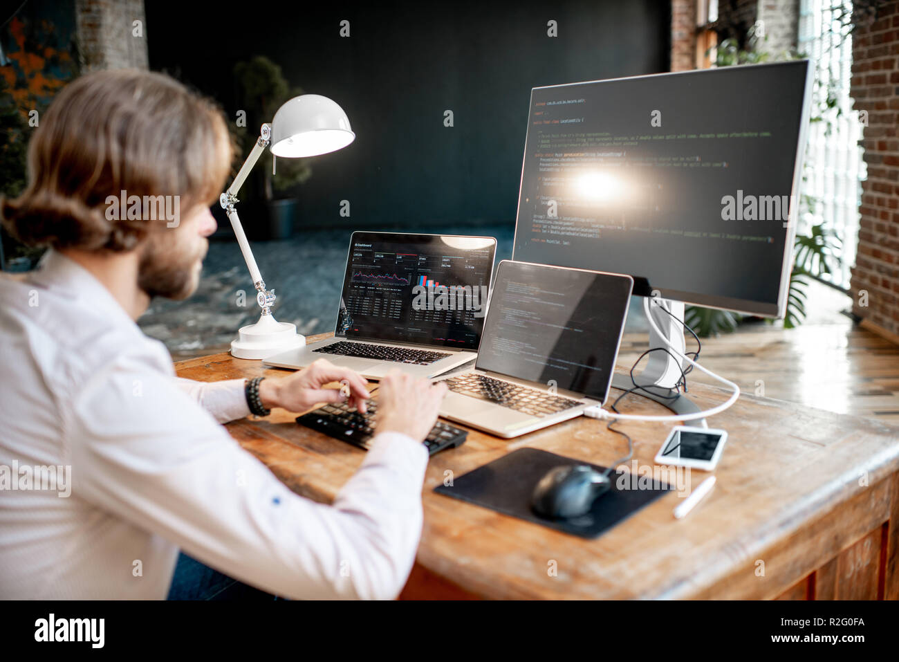 Young male programmer writing a program code sitting at the workplace with three monitors in the office. Image focused on the screen Stock Photo
