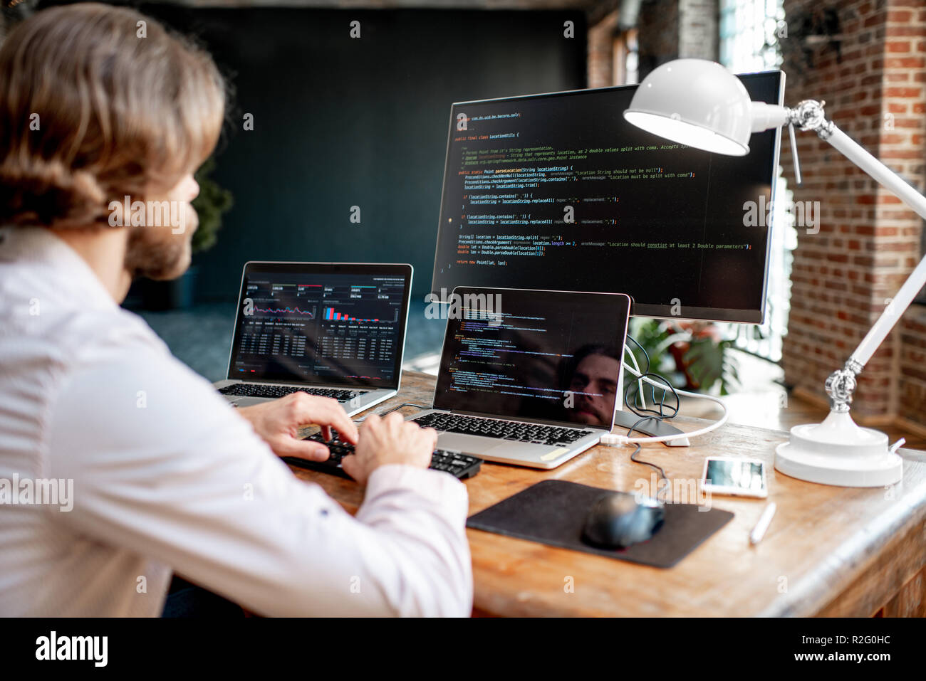Young male programmer writing a program code sitting at the workplace with three monitors in the office. Image focused on the screen Stock Photo