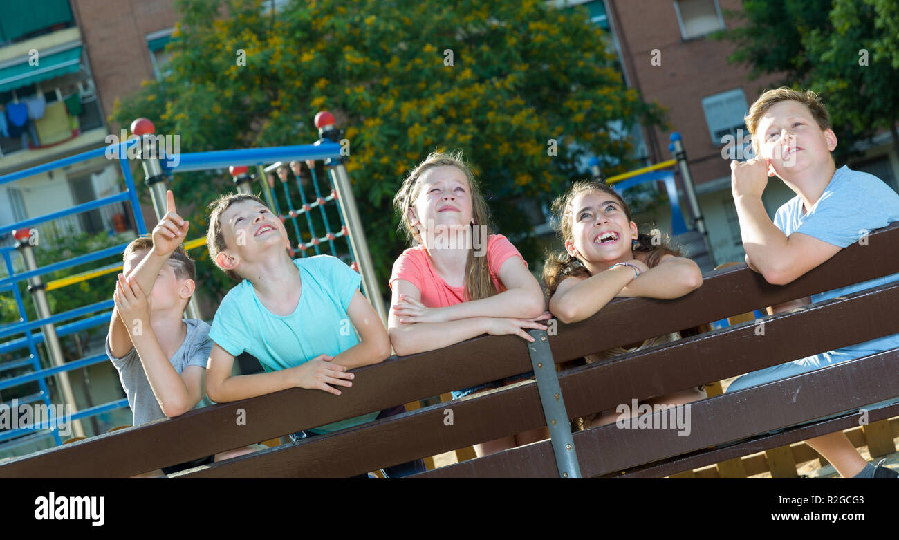 Five glad children sitting on a bench at the playground and point to ...