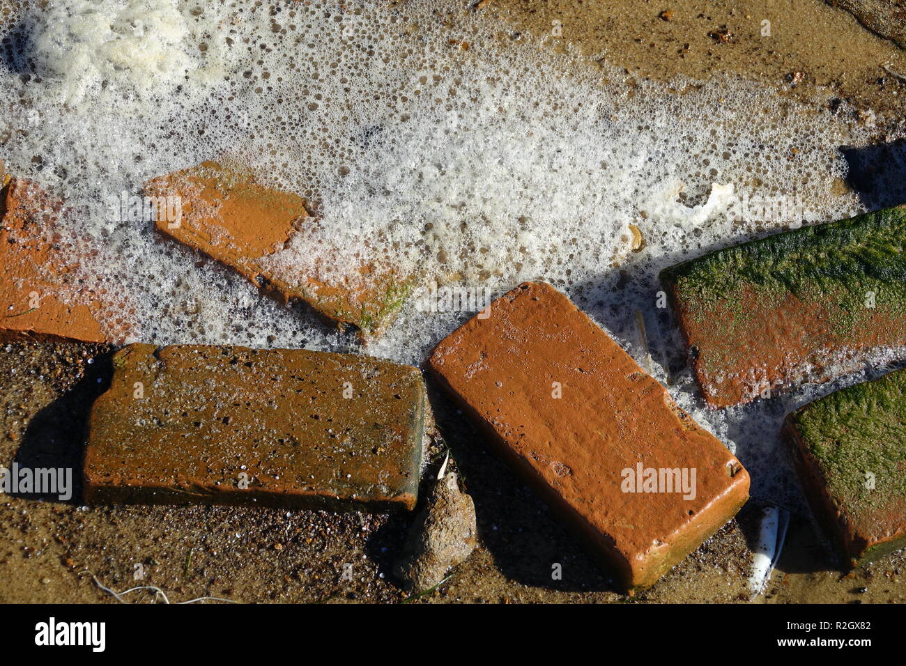 red bricks from eroded colonial era well with green algae and wave foam Stock Photo