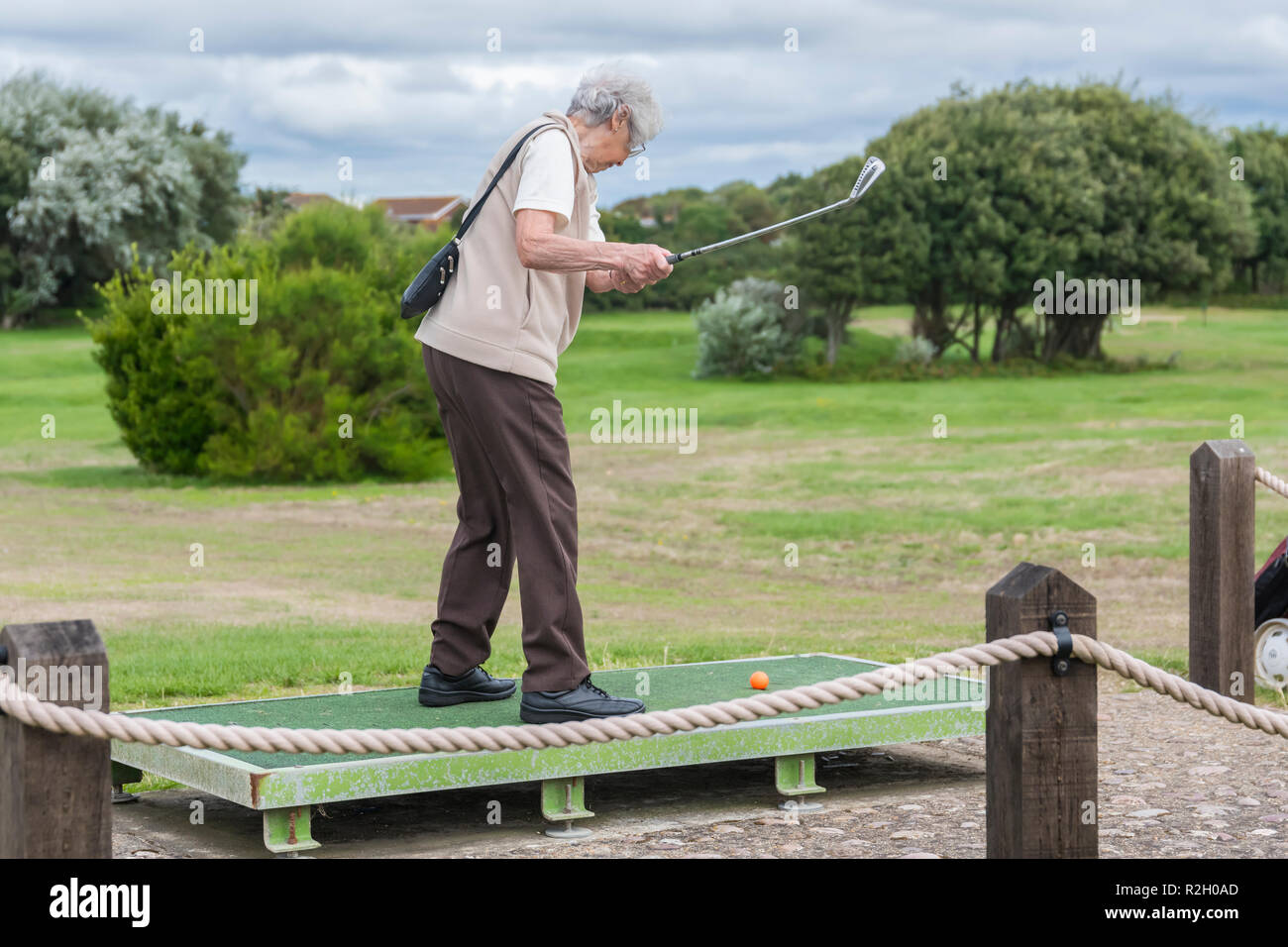 Senior woman swinging a golf club as she plays mini golf on a course in the UK. Elderly lady playing sport. Stock Photo