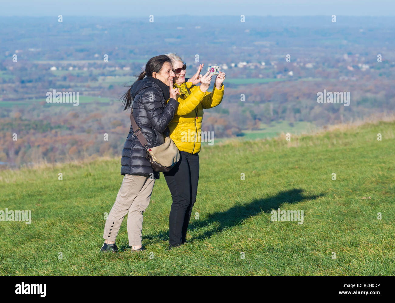 Pair of middle aged female friends taking a selfie photo while making V signs in the British countryside on a hill in the UK. Stock Photo