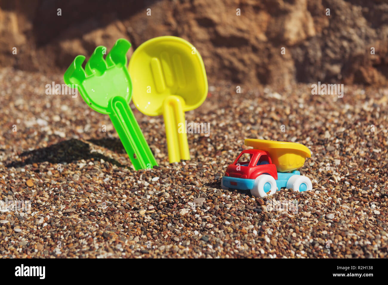 Children's toy truck with gravel or sand. Yellow scoop and green rake on the background. Concept of transportation of goods and building materials. In Stock Photo