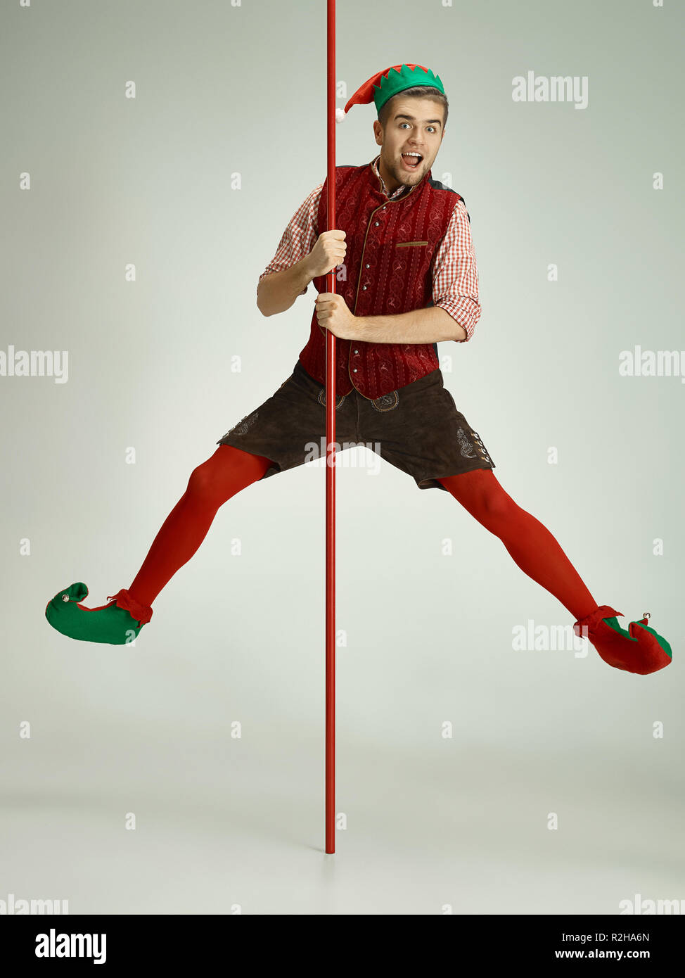 The happy smiling friendly man dressed like a funny gnome or elf posing on an isolated gray studio background. The winter, holiday, christmas concept Stock Photo