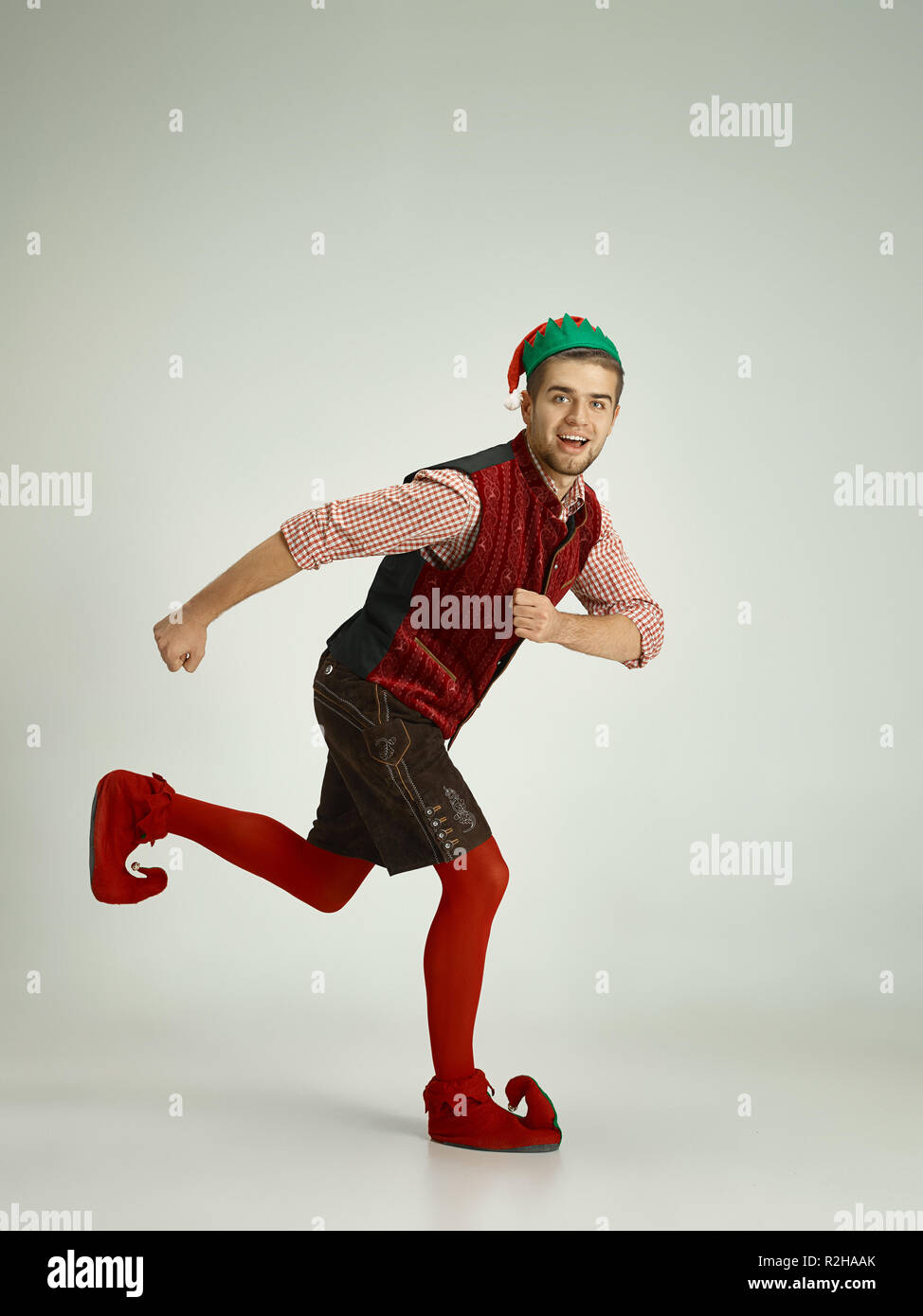 The happy smiling friendly man dressed like a funny gnome or elf running on an isolated gray studio background. The winter, holiday, christmas concept Stock Photo