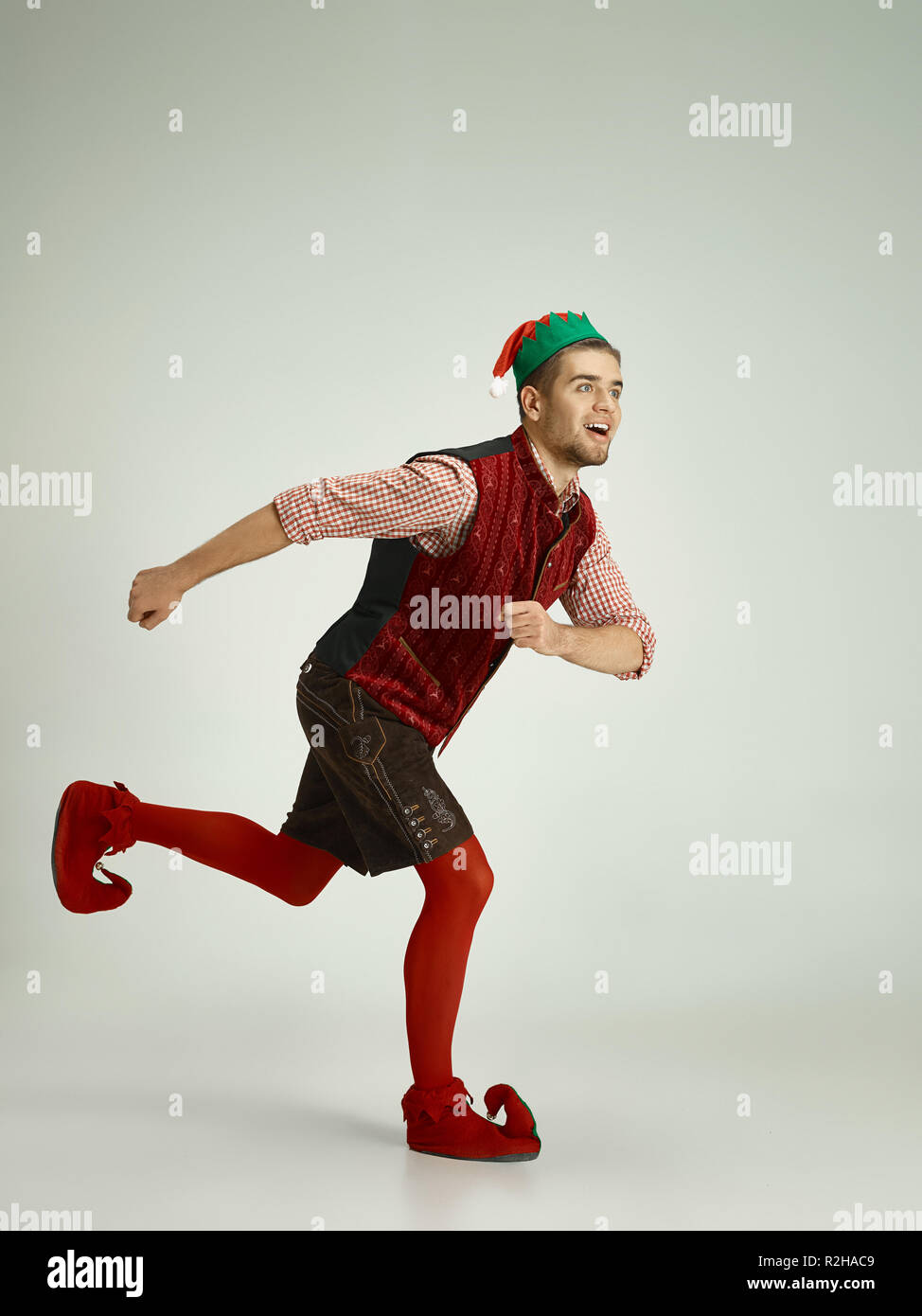 The happy smiling friendly man dressed like a funny gnome or elf running on an isolated gray studio background. The winter, holiday, christmas concept Stock Photo