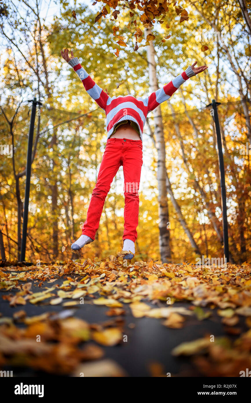 Boy jumping on a trampoline covered in autumn leaves, United States