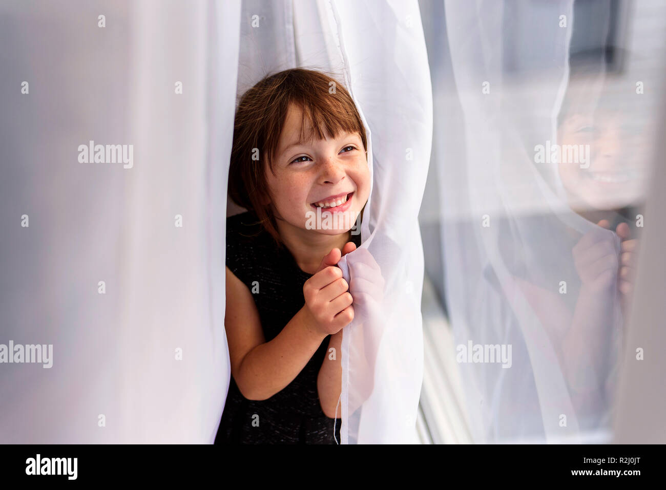 Girl hiding behind a curtain laughing Stock Photo