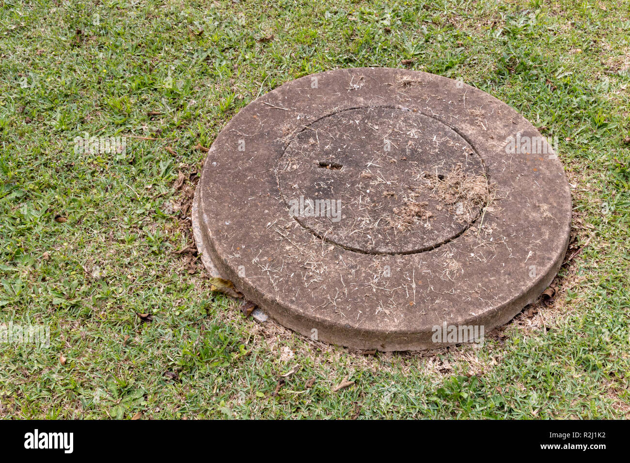 A close up view of a concrete man hole cover over the water system with dried grass that has been cut around it Stock Photo
