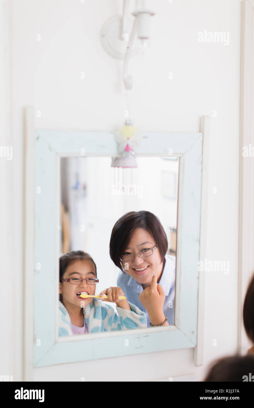Mother watching daughter brushing teeth in bathroom mirror Stock Photo