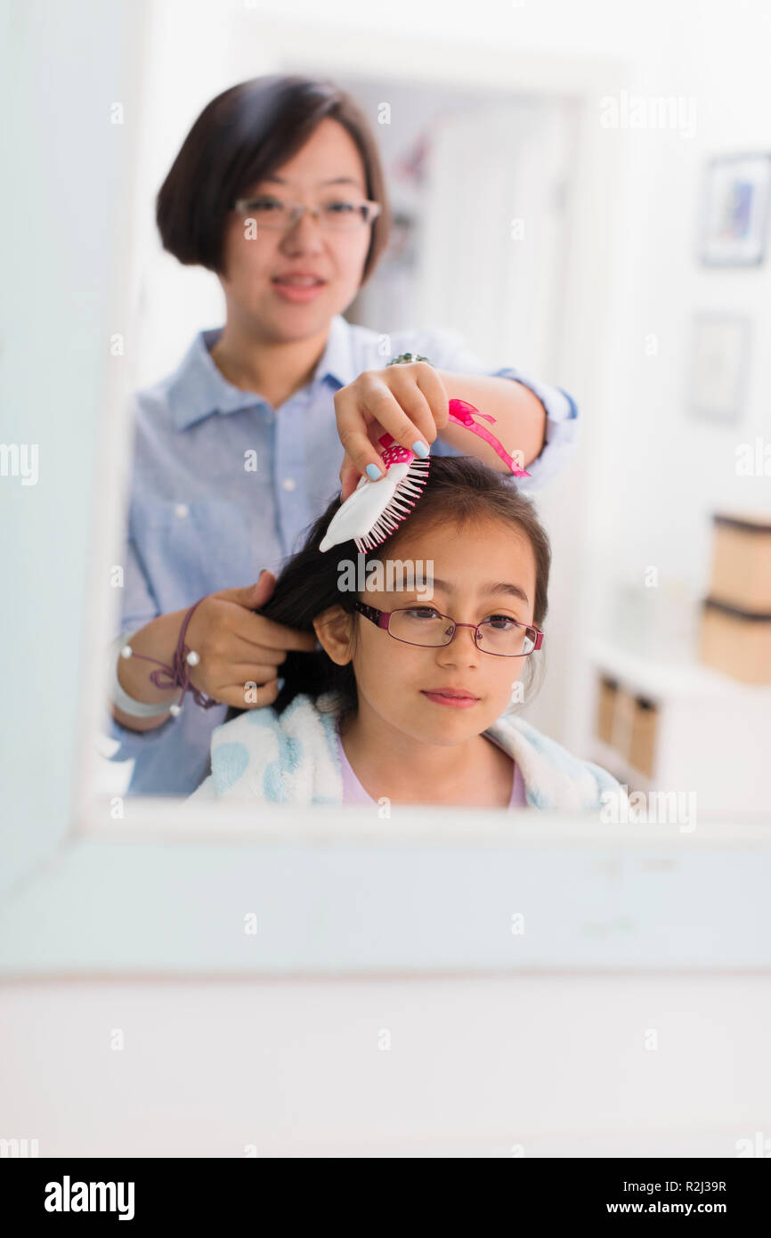 Mother brushing daughters hair in bathroom mirror Stock Photo