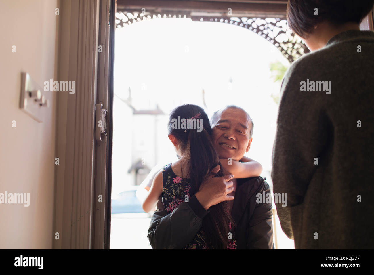 Affectionate granddaughter greeting and hugging grandfather in doorway Stock Photo