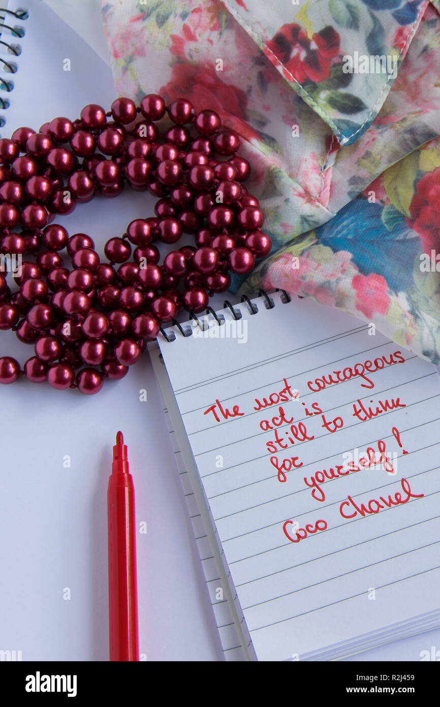 Coco Chanel quotes written on a block note, pearl accessories and and silky  flower shirt ,inspiration phrase "The most courageous act is still to thi  Stock Photo - Alamy
