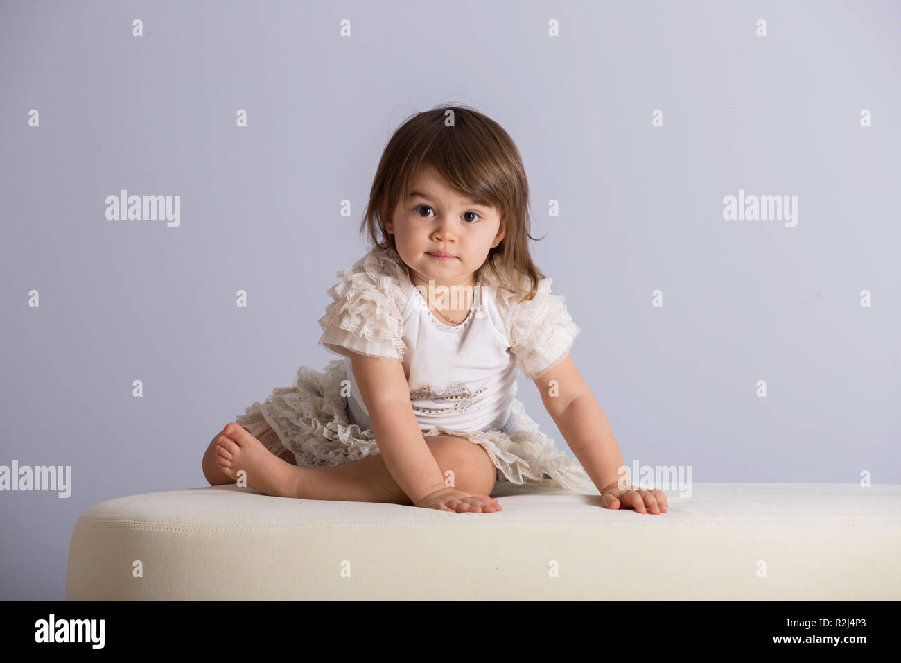 Pretty Baby Girl With Brown Hair In White Dress On Light Purple