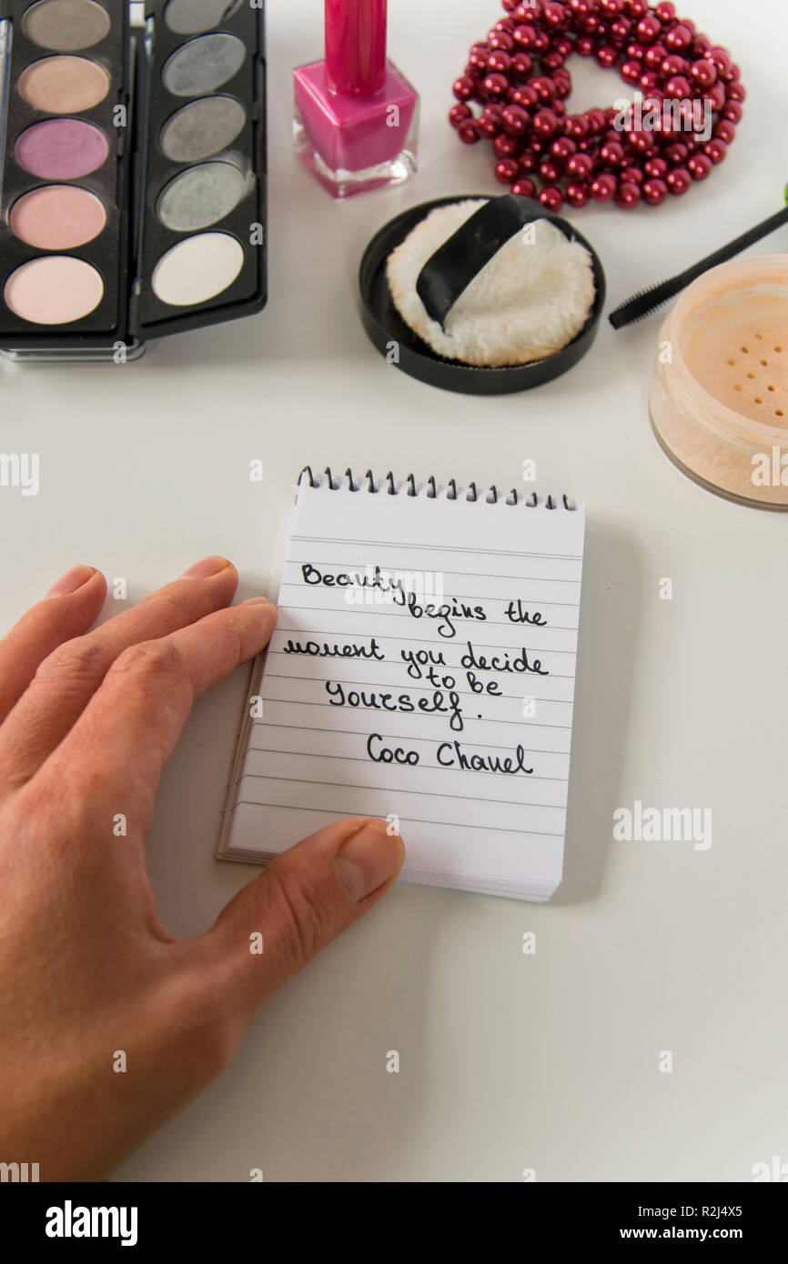 Woman hand holds Coco Chanel quotes written on a block note, pearl