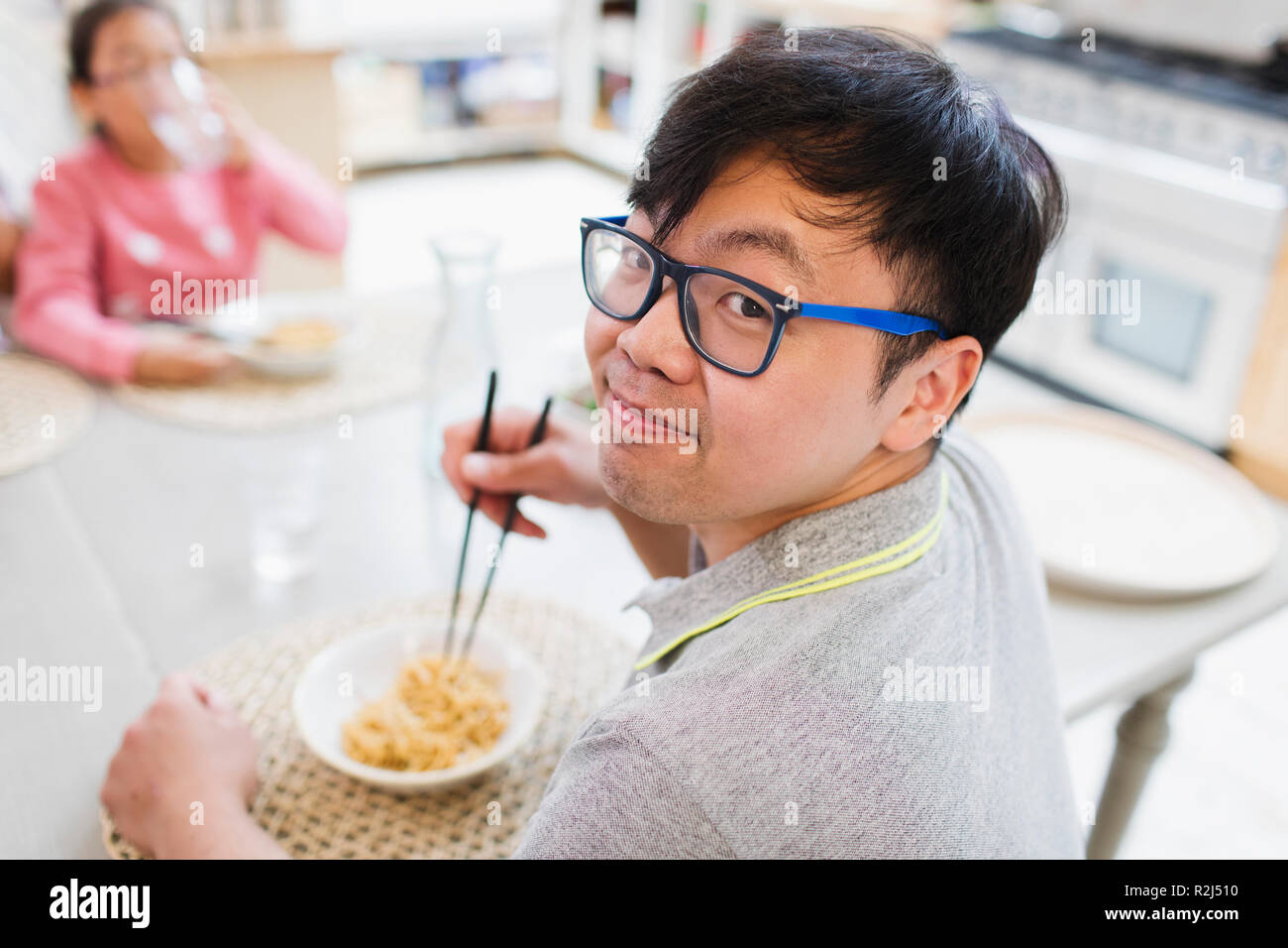 Portrait smiling man eating noodles with chopsticks at table Stock Photo