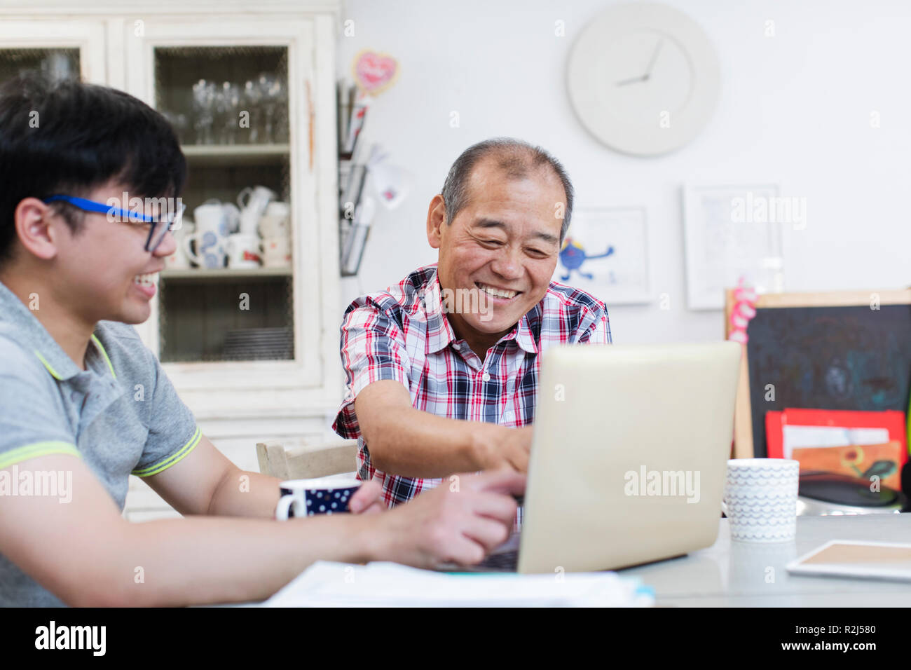Son helping senior father using laptop in kitchen Stock Photo