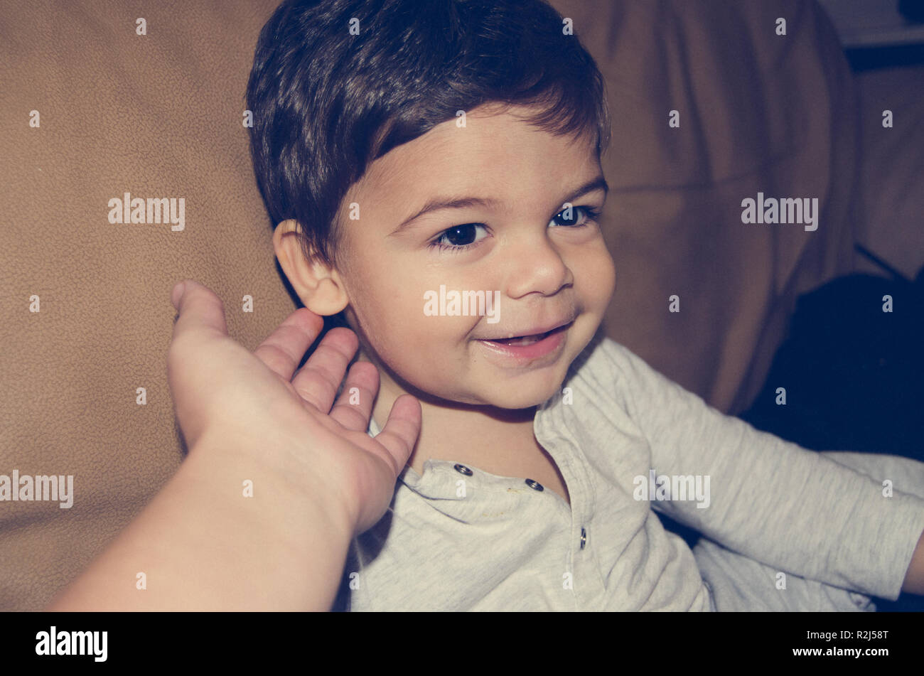 Mother cuddling one year old baby boy with long black hear on his cheek