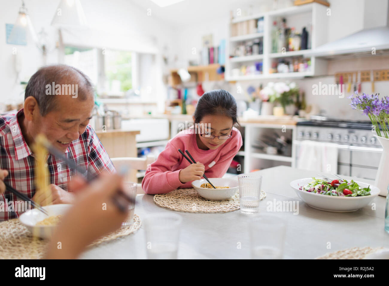 Grandfather and granddaughter eating noodles with chopsticks at table Stock Photo