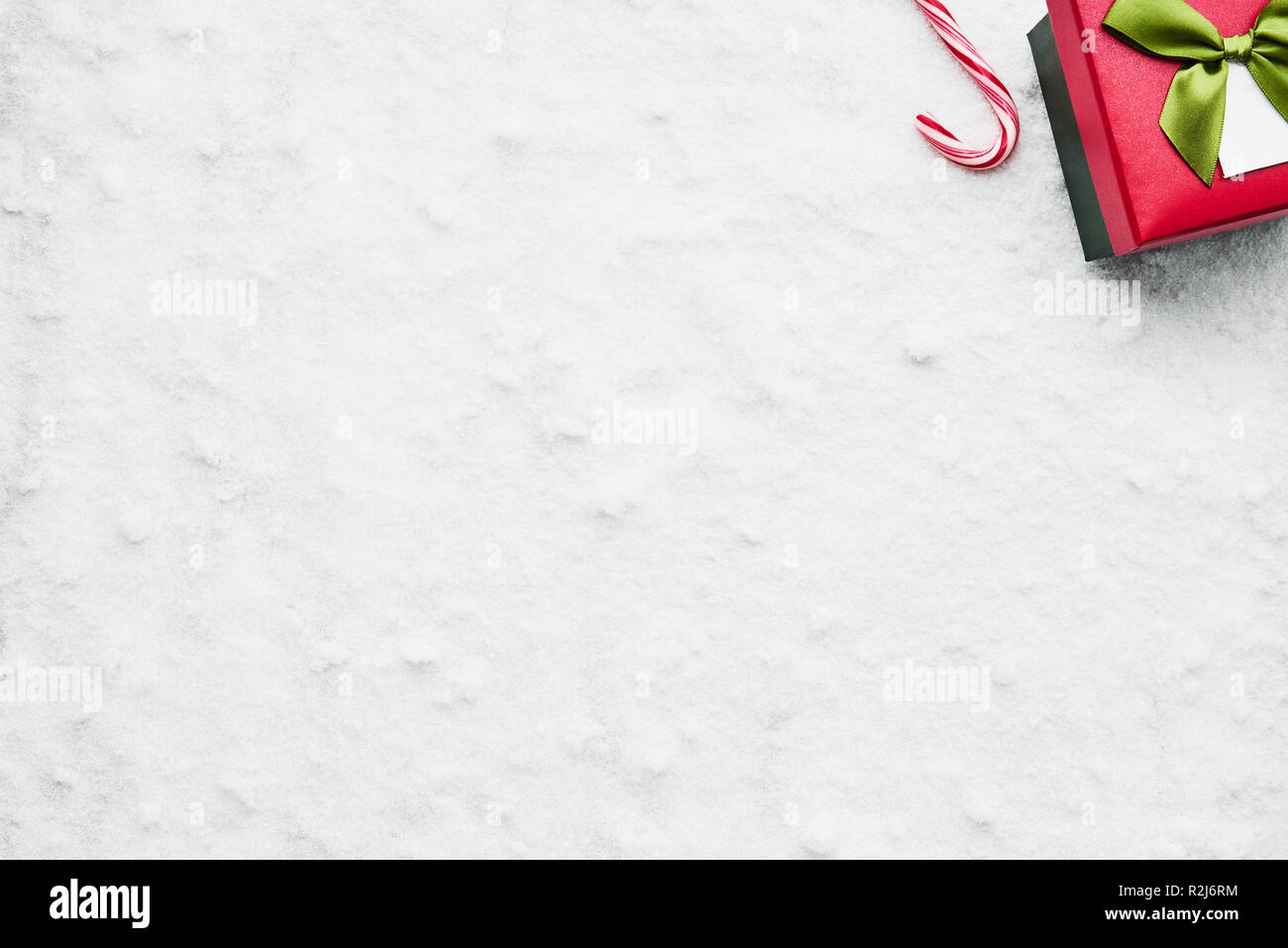 Top view of green and red Christmas gift box with ribbon and candy cane on the snow. Copy space for text. Stock Photo