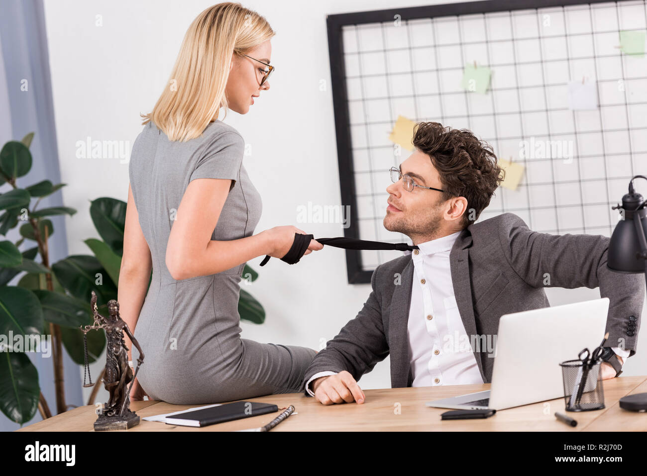 young businesswoman pulling colleagues tie while sitting on table in office,  office romance concept Stock Photo - Alamy