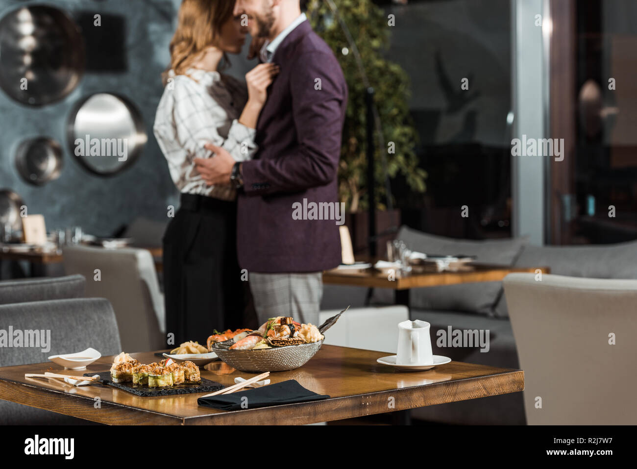 Partial view of beautiful hugging couple dancing behind the table served with sushi in restaurant Stock Photo