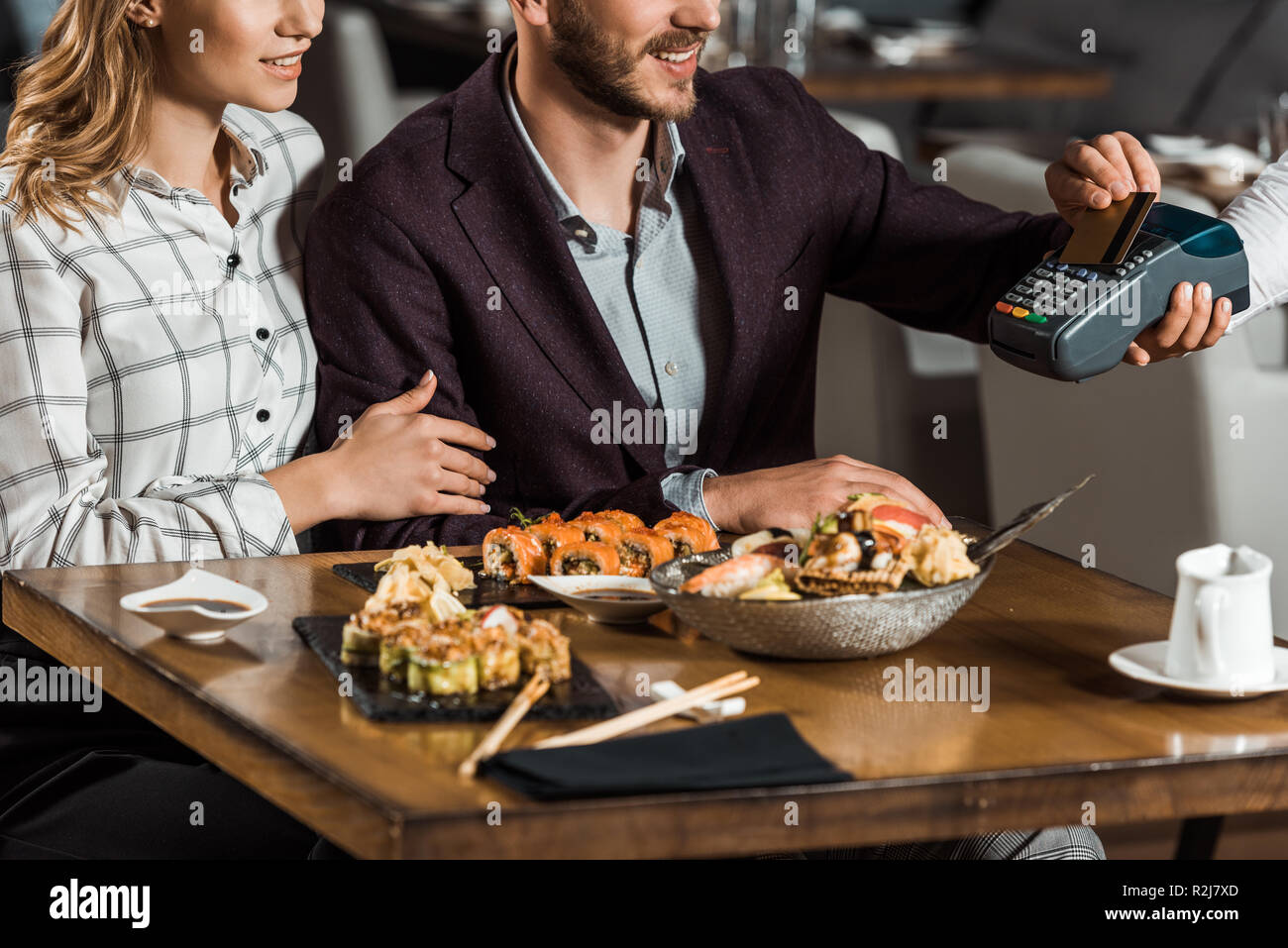 Partial view of couple sitting at table while man paying for dinner in restaurant Stock Photo