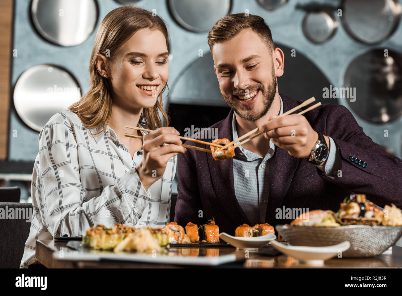 Smiling attractive young adult couple eating sushi together in restaurant Stock Photo