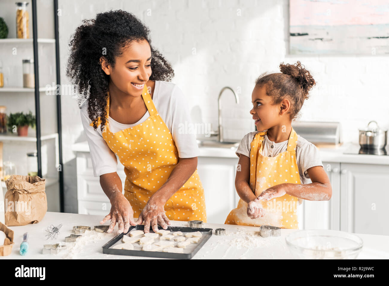 smiling african american mother and daughter preparing cookies and looking at each other in kitchen Stock Photo