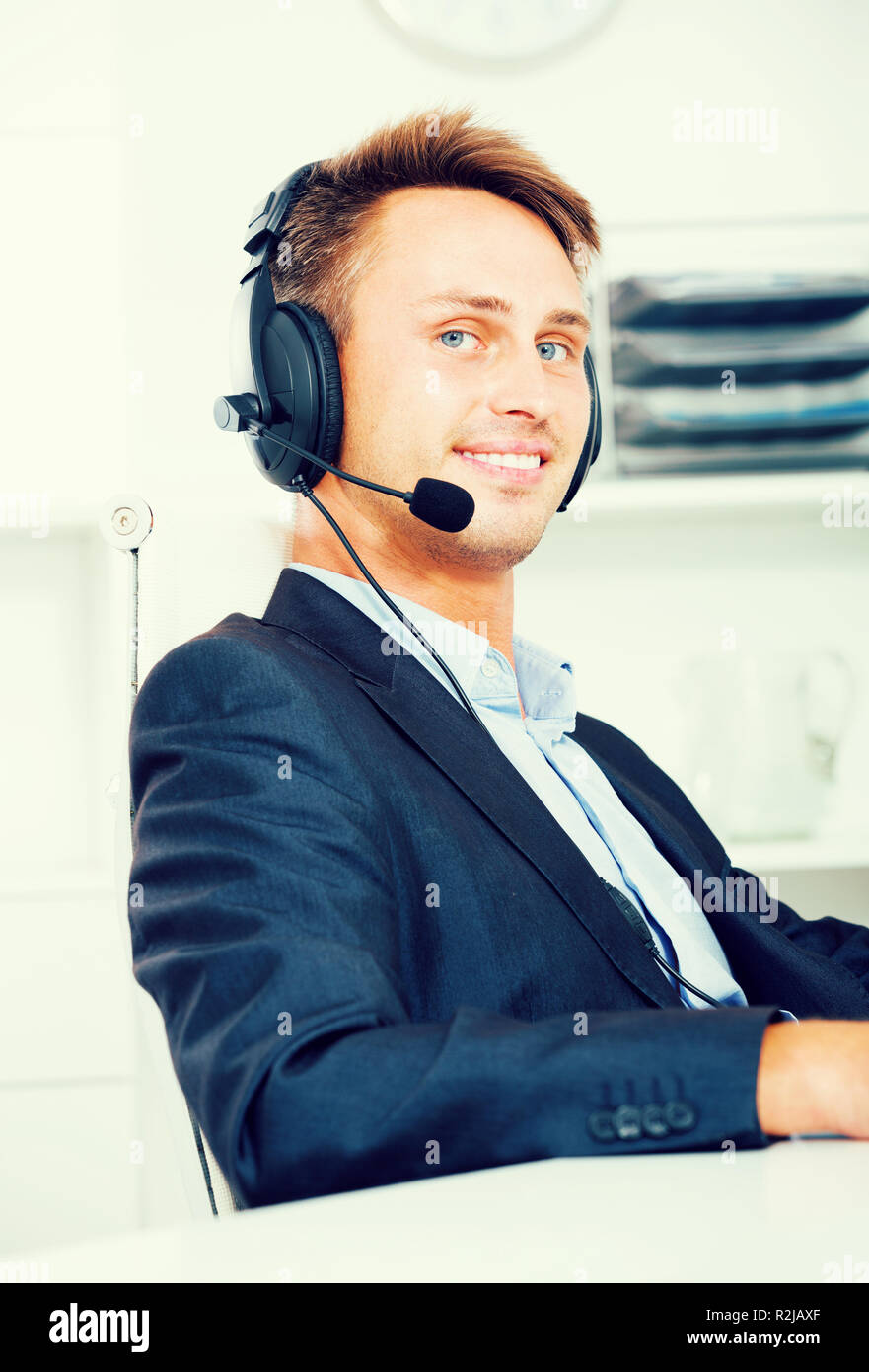 Cheerful young man talking using hands-free set at customer service office Stock Photo