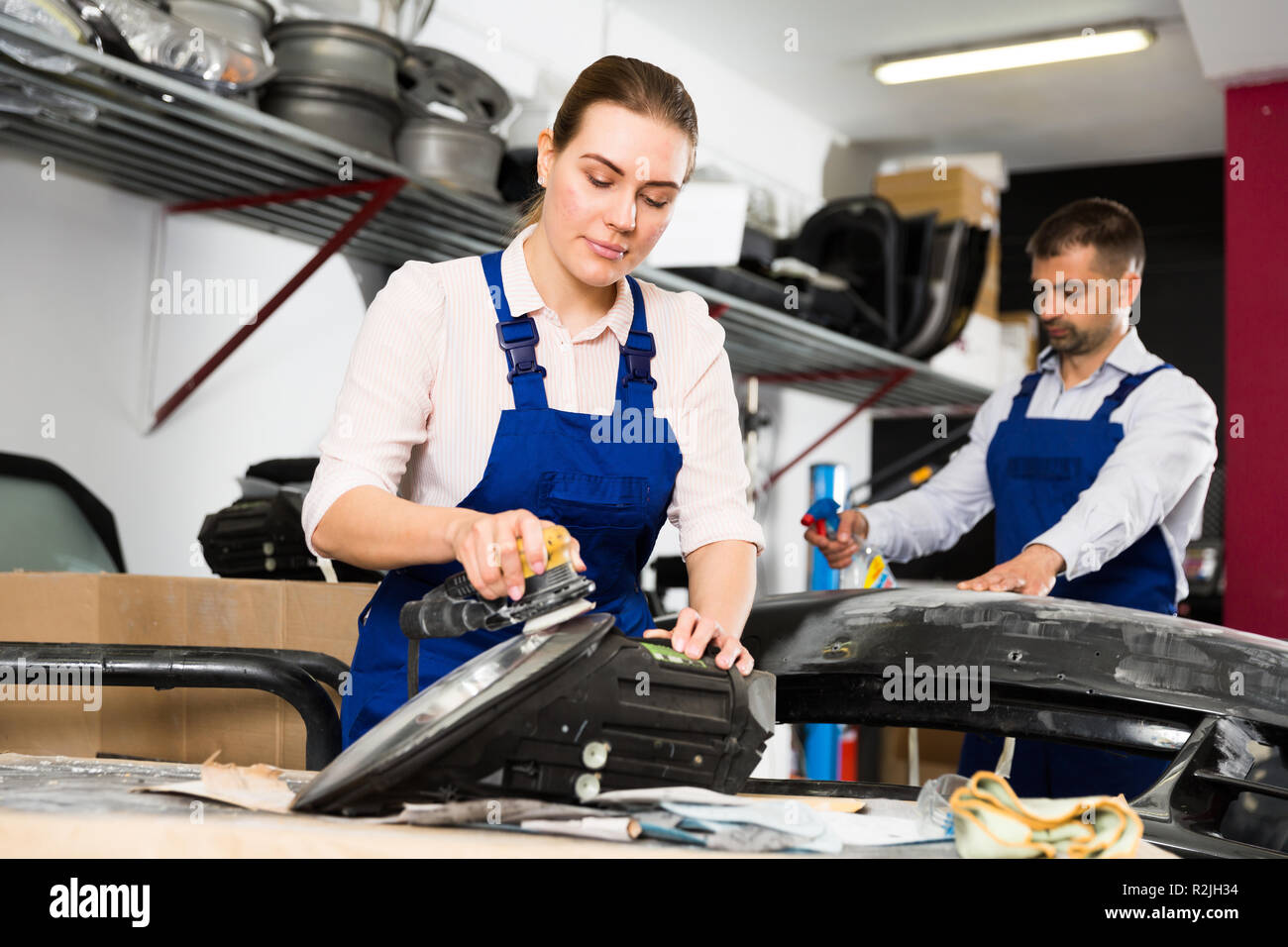 Professional female worker polishing headlamp in auto repair shop Stock Photo